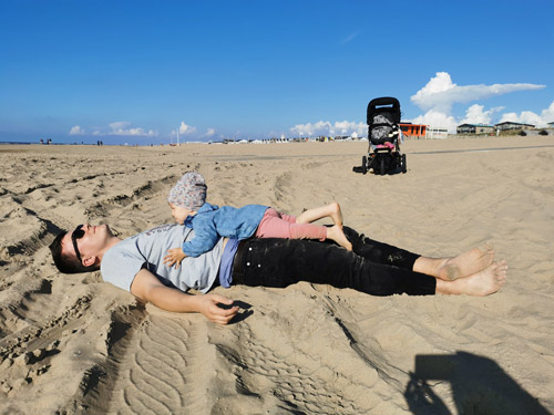 Me lying clothed on a beach and my daughter lying on top of me looking at me